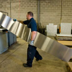 A Matot shop worker carries a sheet of metal to be used on a new dumbwaiter.